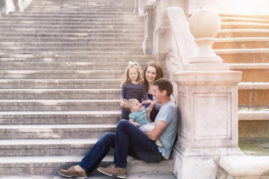 a family is sitting on the stairs next to a fountain .