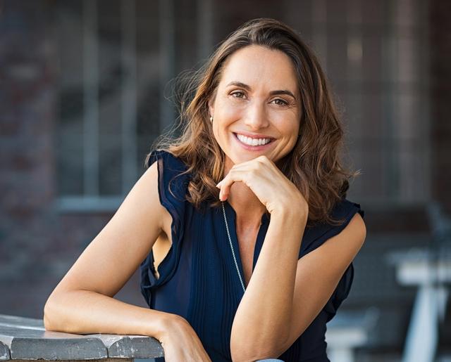 a woman is sitting at a table with her hand on her chin and smiling .