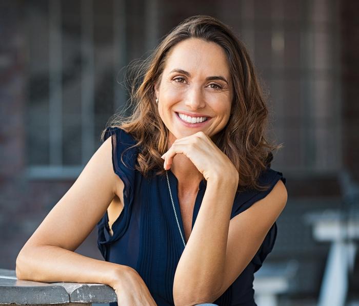 a woman is sitting at a table with her hand on her chin and smiling .