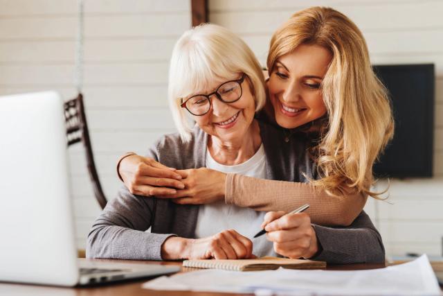 a woman is hugging an older woman while she writes in a notebook .