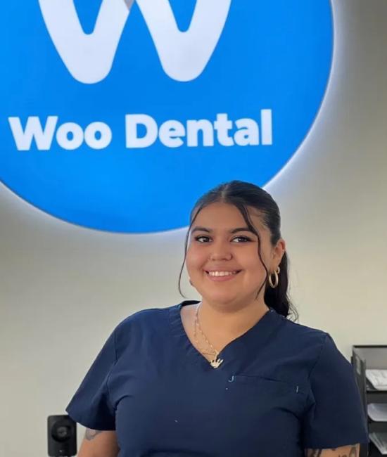 a woman in a scrub top is smiling in front of a woo dental sign .