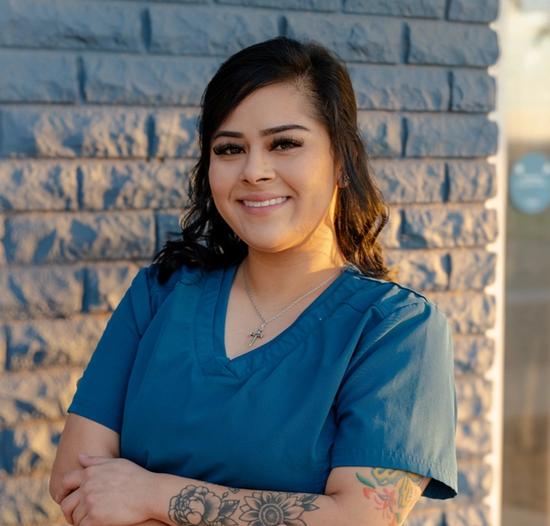 a woman in a blue scrub top with a tattoo on her arm is standing in front of a brick wall .