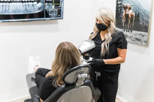 a woman is sitting in a dental chair while a dentist looks at her teeth .