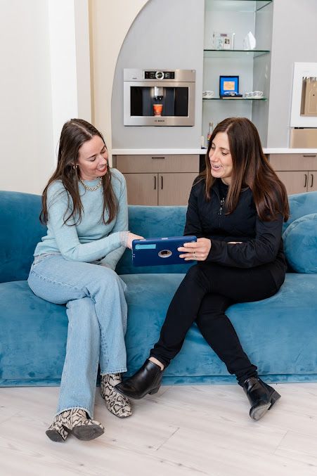 a woman is sitting on a blue couch looking at a tablet .