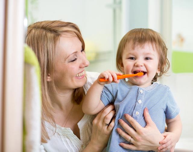 Mother smiling while holding a happy toddler brushing teeth.