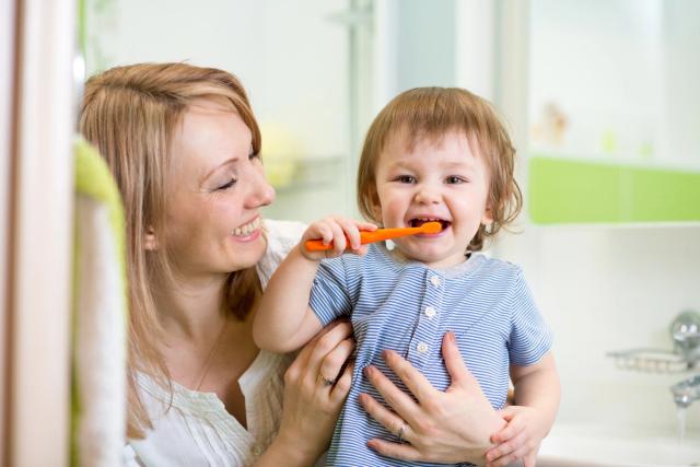 a woman is holding a baby who is brushing his teeth in front of a mirror .
