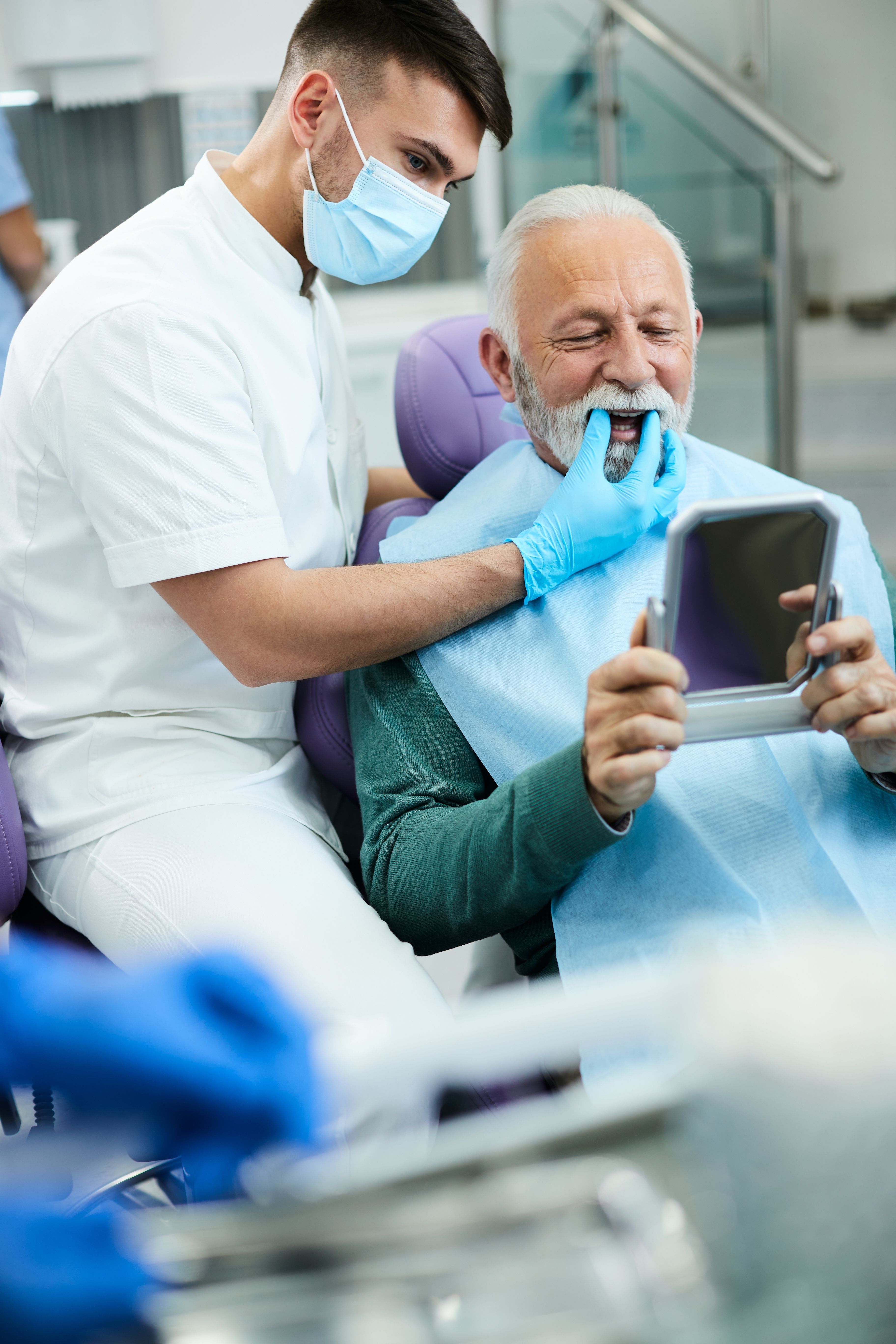 an elderly man is looking at his teeth in a mirror at the dentist 's office .