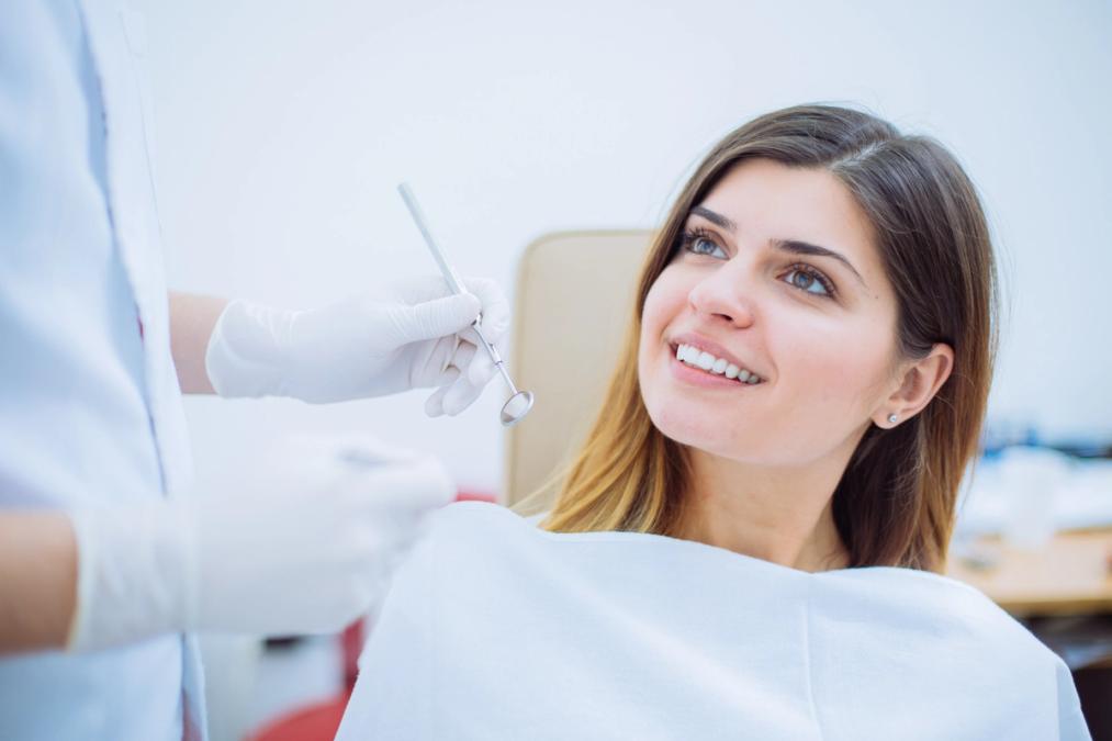 Smiling woman in a dental chair looking at a dentist holding a dental mirror.