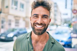 A smiling man with a beard wearing a green shirt in a city.