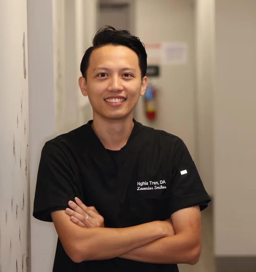 a man in a black scrub top is leaning against a wall with his arms crossed and smiling .