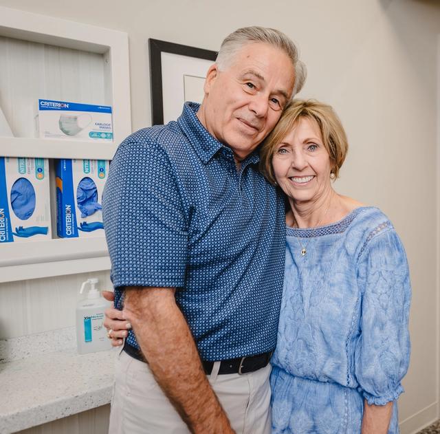a man and woman are posing for a picture in front of a shelf with gloves on it .