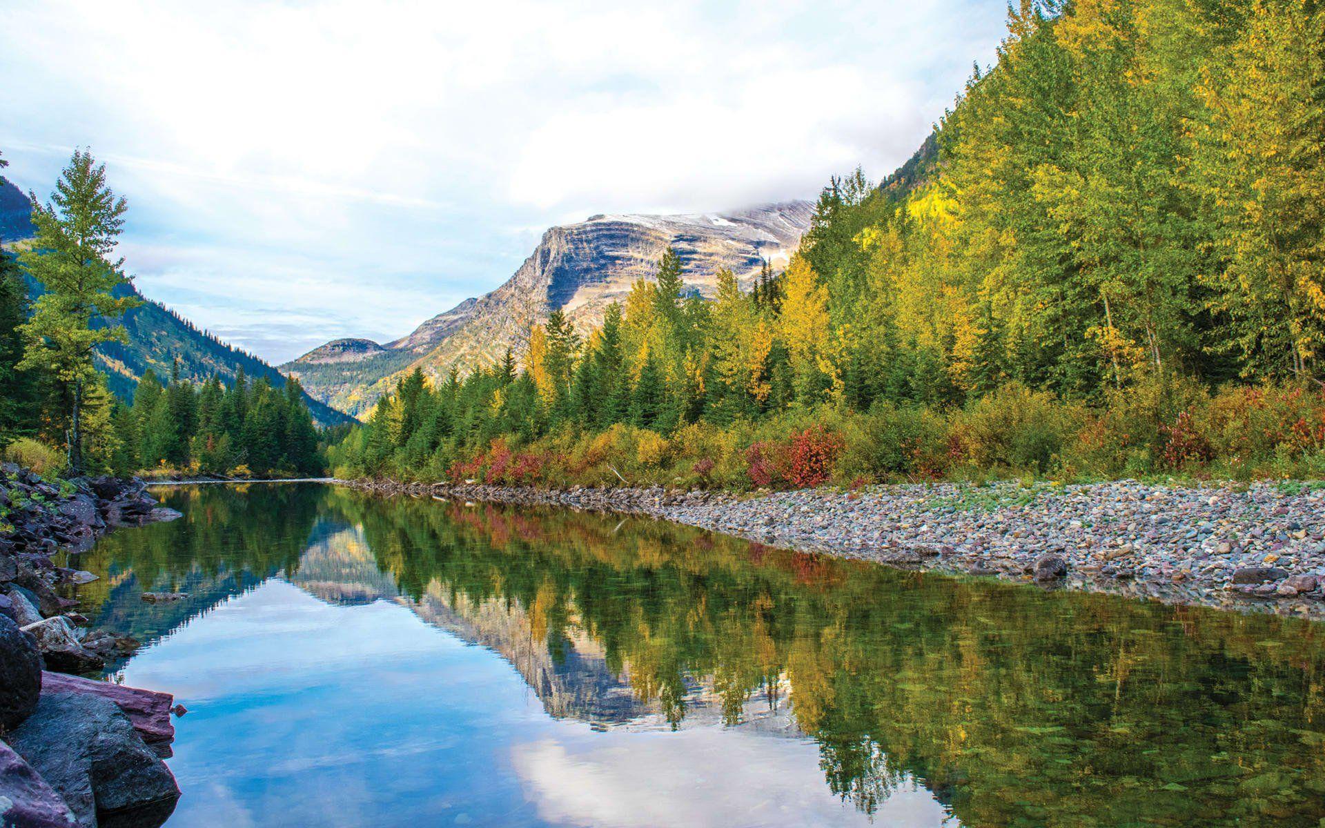 a river surrounded by trees and mountains is reflected in the water .