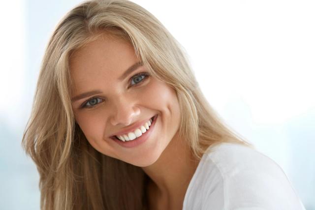 a woman with blonde hair and blue eyes is smiling and looking at the camera .