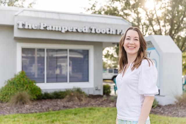 Smiling woman stands in front of The Pampered Tooth PA building.