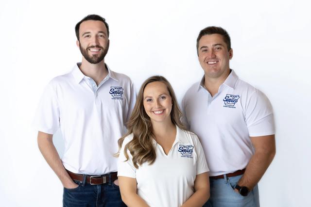 three people wearing white polo shirts are posing for a picture .