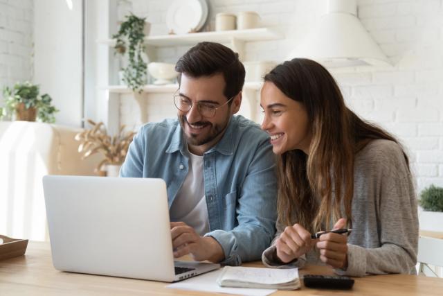 a man and a woman are sitting at a table looking at a laptop computer .