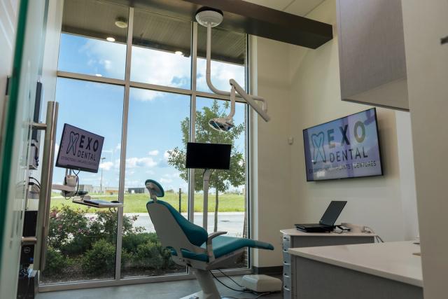 a dental office with a dental chair , monitors , and a large window .
