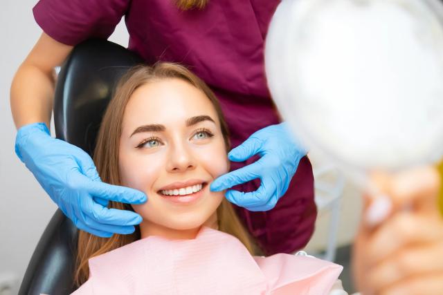 a woman is sitting in a dental chair looking at her teeth in a mirror .