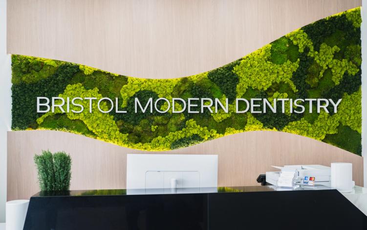 Modern reception area with "BRISTOL MODERN DENTISTRY" on a wavy green moss wall above a black desk.