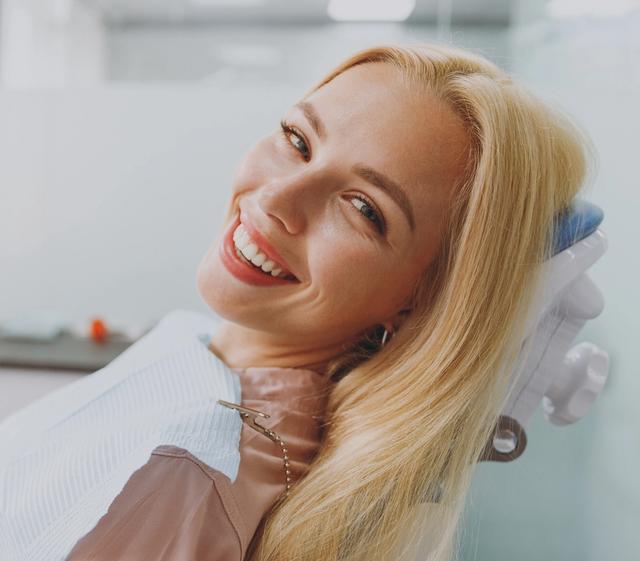 a woman is smiling while sitting in a dental chair .