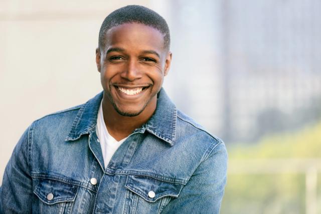 a young man in a denim jacket is smiling for the camera .