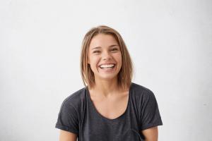 A young woman with short brown hair laughs heartily, looking at the camera against a white background.
