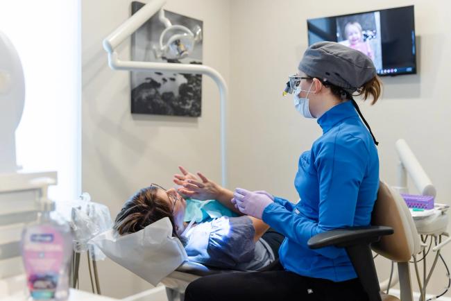 A dentist wearing a mask and loupes works on a patient in a dental chair.