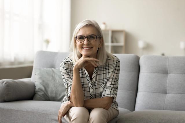 an elderly woman is sitting on a couch wearing glasses and smiling .