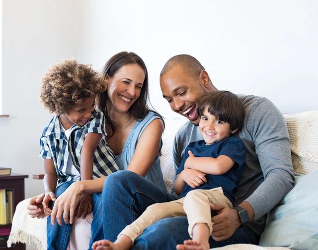 A happy family of four, including two parents and two young children, sitting together and smiling.