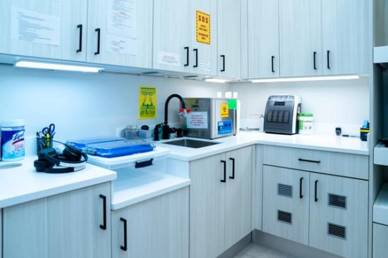 A clean, modern lab workspace with light-colored cabinets, white counters, a sink, and various equipment.