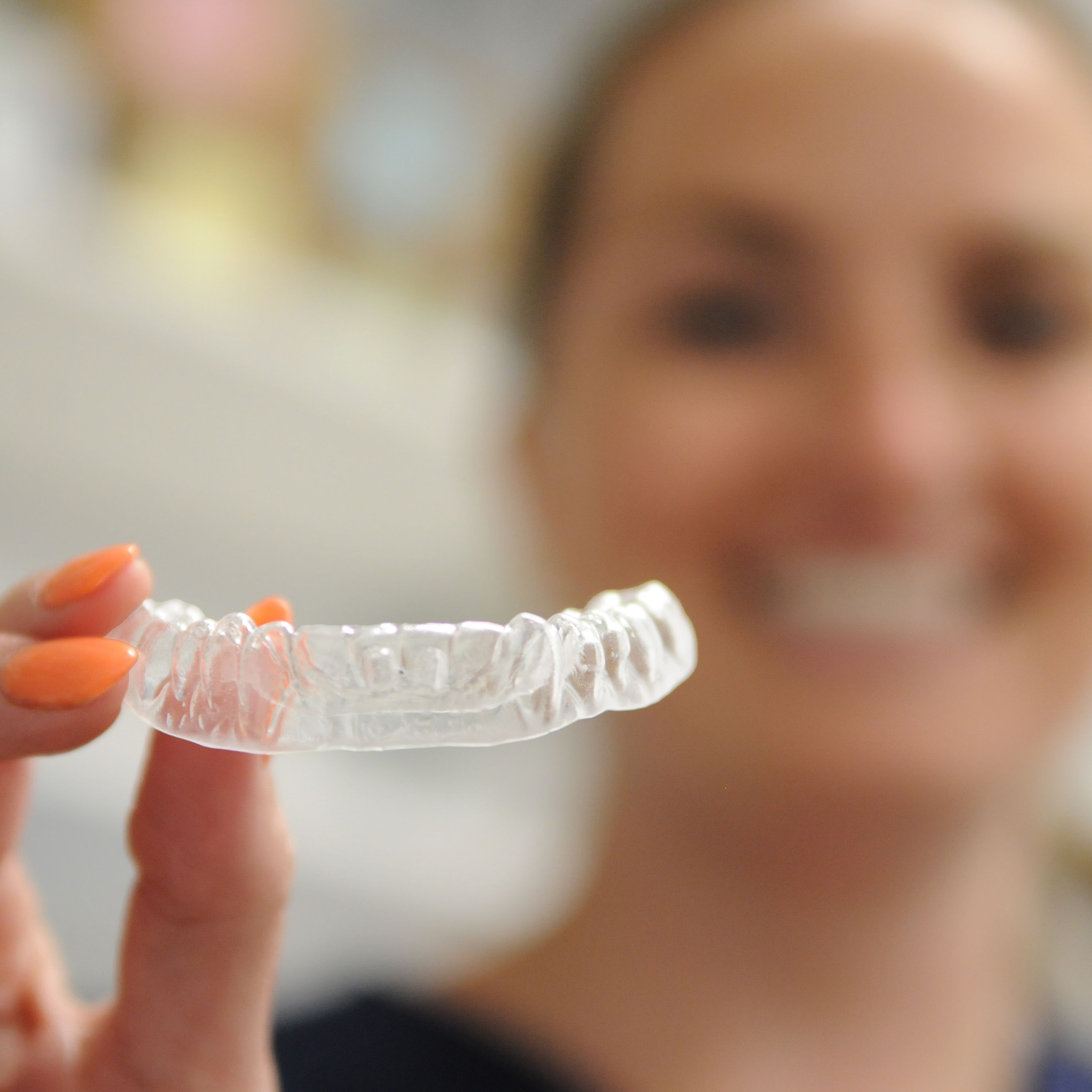 a woman is smiling while holding a clear retainer in her hand .