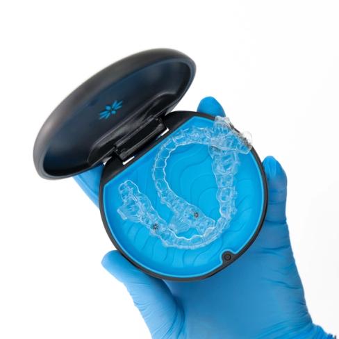 a person wearing blue gloves is holding a case with a clear brace in it .