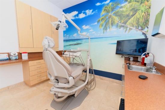 a dental office with a dental chair , sink , and television .