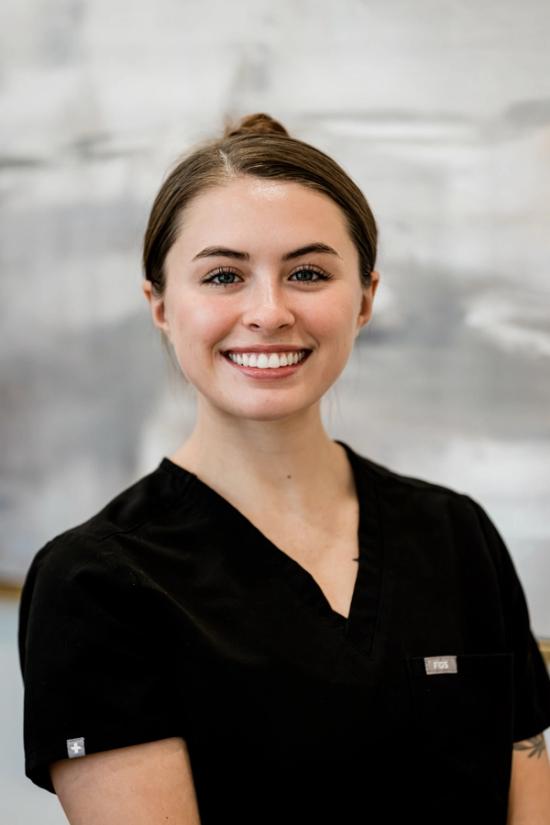 A smiling young woman in black scrubs.
