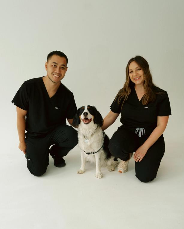 a man and a woman kneeling next to a black and white dog