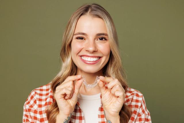 a woman is smiling while holding a clear braces .