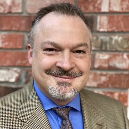 a man in a suit and tie is smiling in front of a brick wall .
