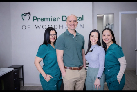 Four smiling staff members, two in scrubs, standing in front of the 'Premier Dental of Woodhaven' sign.