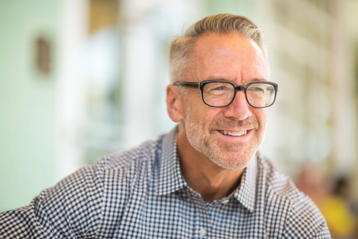 a man wearing glasses and a plaid shirt smiles