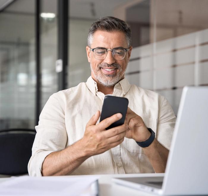 a man is sitting at a desk looking at his cell phone .