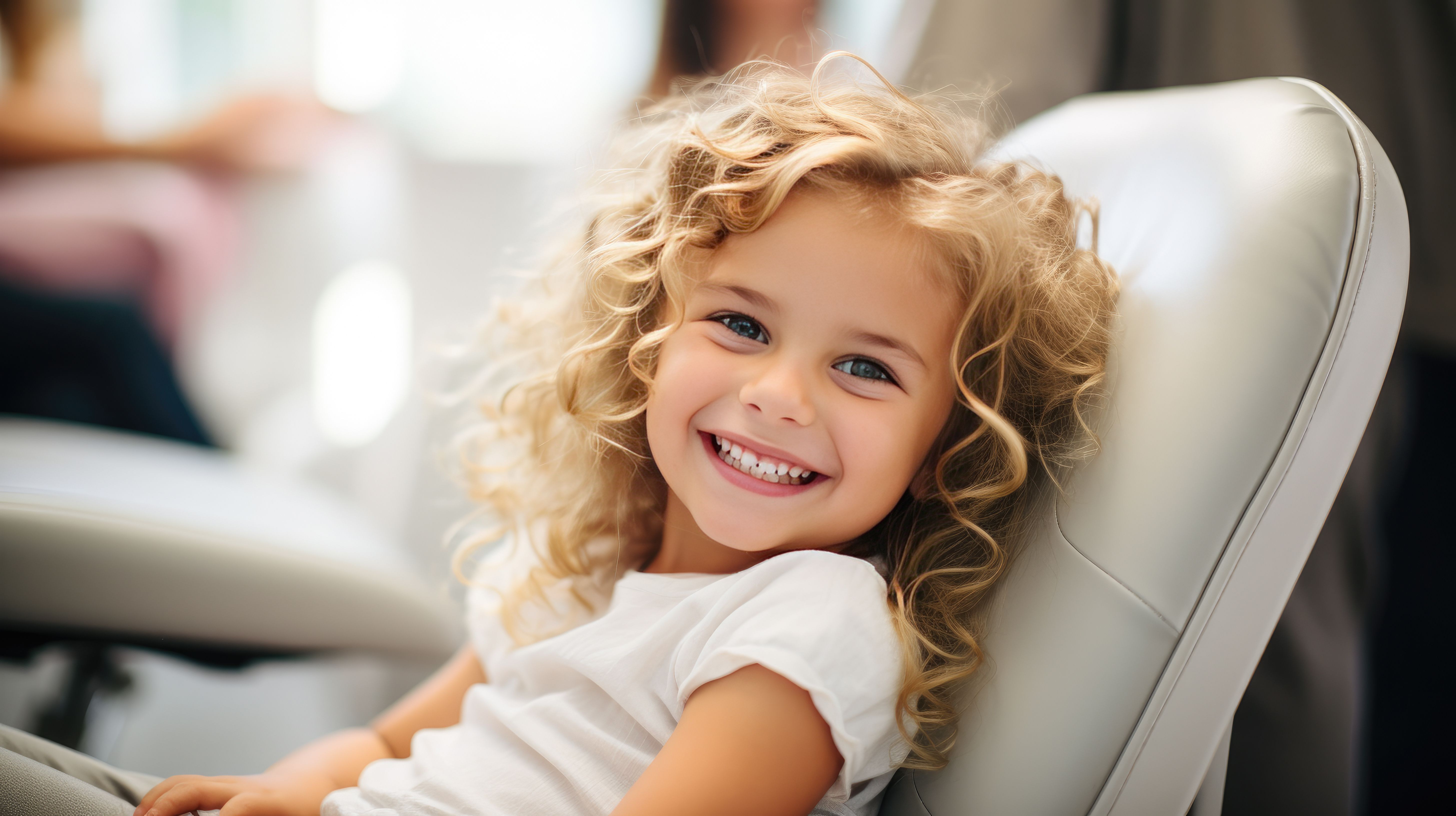 a little girl with curly hair is sitting in a chair and smiling .