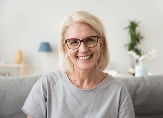 an elderly woman wearing glasses is smiling while sitting on a couch .