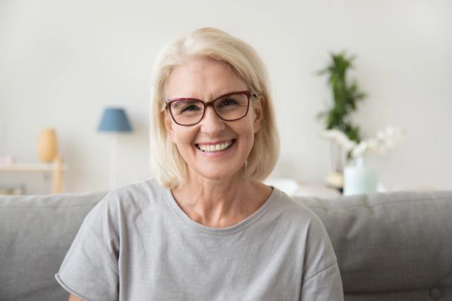 an elderly woman wearing glasses is smiling while sitting on a couch .