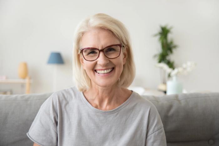 an elderly woman wearing glasses is smiling while sitting on a couch .