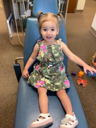 a little girl in a floral dress sits in a dental chair
