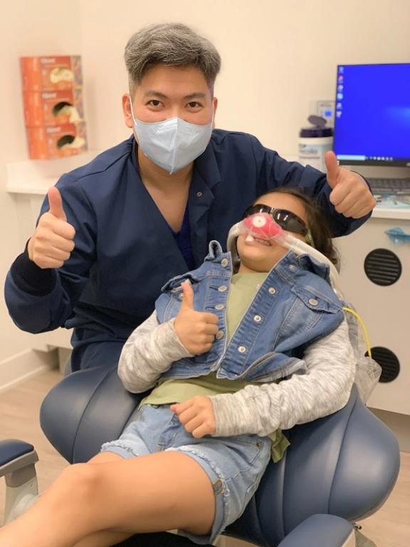 a little girl in a dental chair giving a thumbs up