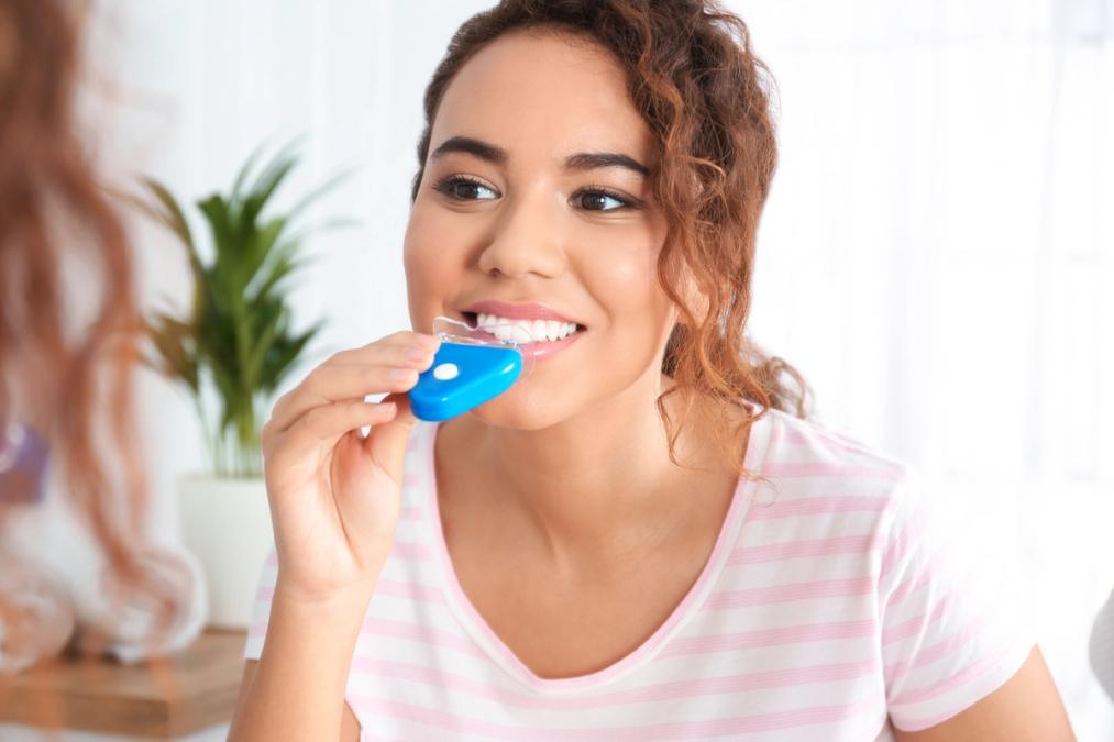 a woman is whitening her teeth in front of a mirror.