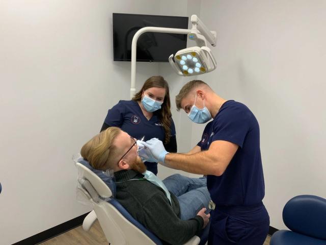 a man is sitting in a dental chair getting his teeth examined by two dentists .