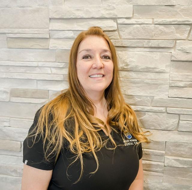 a woman wearing a black dental scrub is smiling in front of a stone wall