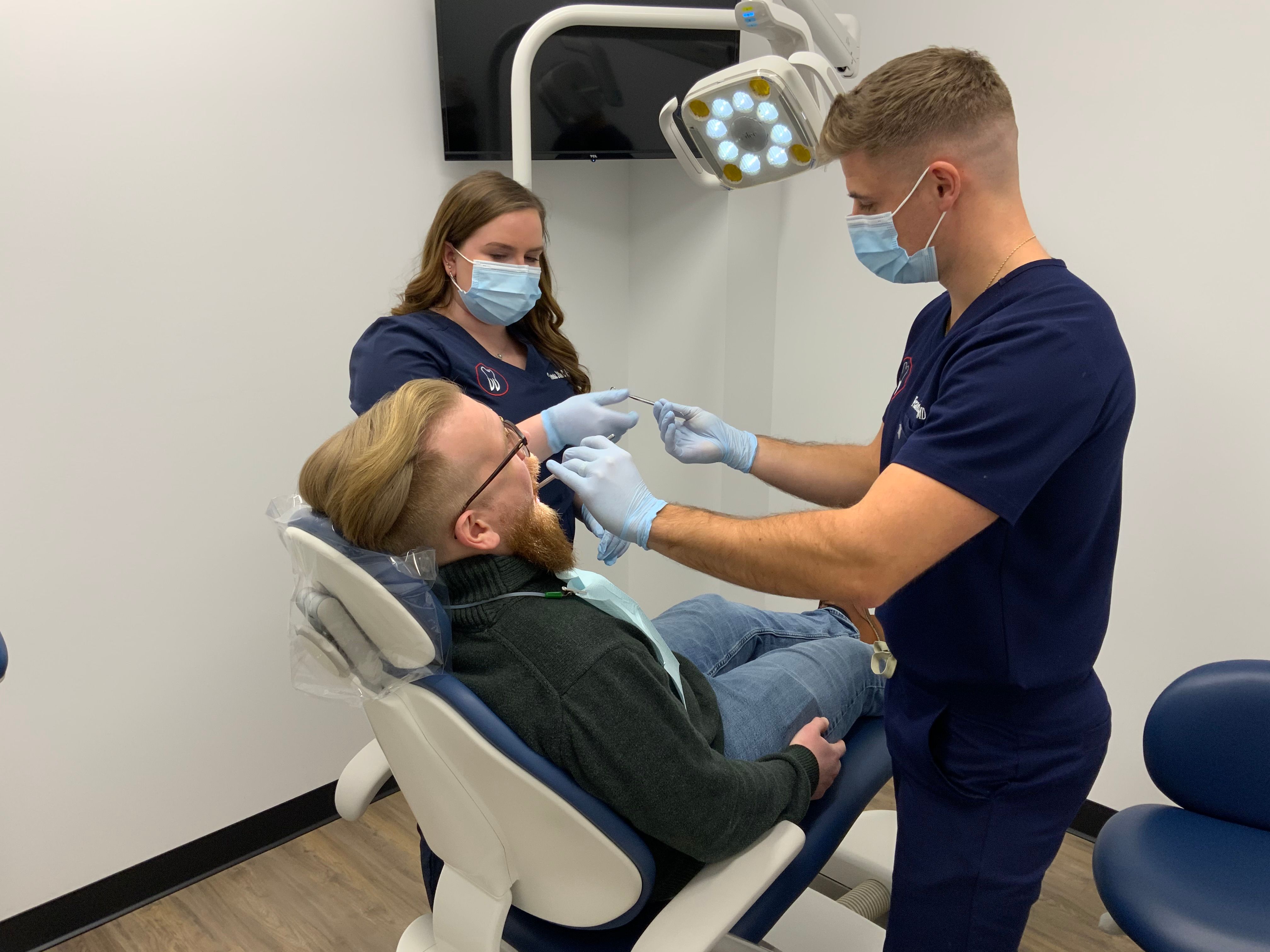 a man is sitting in a dental chair getting his teeth examined by two dentists .